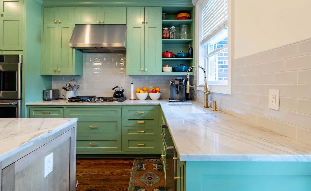 Light green kitchen cabinets with white marble countertops and brass fixtures.