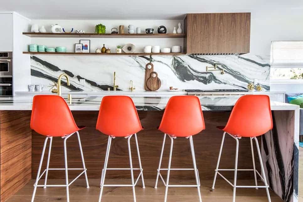 Kitchen with a black and white marble backsplash and vibrant orange bar stools.