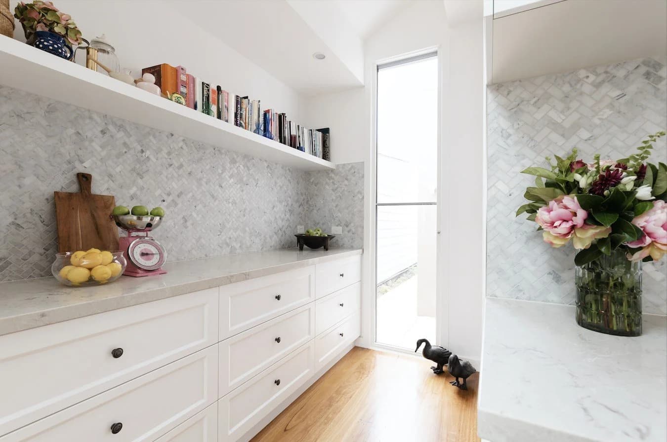 Bright kitchen pantry with white cabinets, light countertops, and herringbone backsplash.