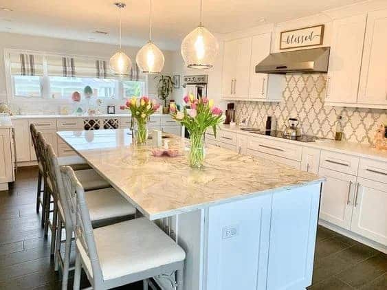 Bright white kitchen with a large island, marble countertops, and floral decor.