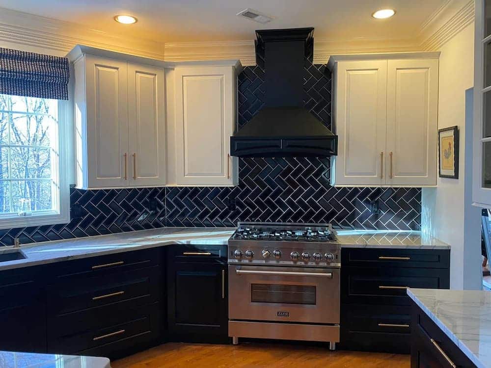 Two-tone kitchen with black and white cabinets and black herringbone backsplash.